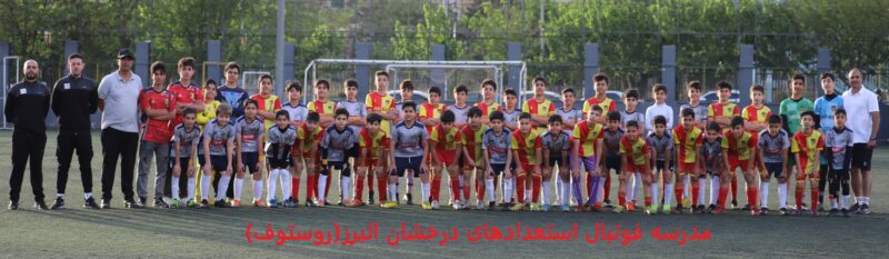 عکس گروهی از یک تیم فوتبال نوجوانان در کرج، شامل 25 بازیکن با لباس‌های متنوع (زرد، قرمز، آبی و خاکستری) با لوگوی "Rosto"، ایستاده و نشسته در زمین چمن، همراه با سه مربی با لباس‌های ورزشی، با متن فارسی "مدرسه فوتبال استعدادهای درخشان" در پایین، نمایش‌دهنده اتحاد و آموزش فوتبالی حرفه‌ای در محیطی سبز و پویا